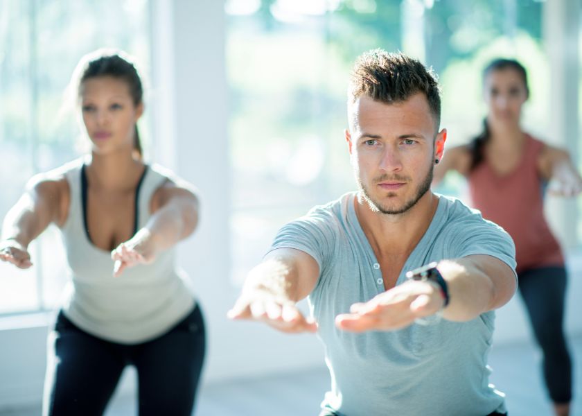 People in a bright fitness class do squats, focusing on movement, flexibility, and joint health supported by E3Live.