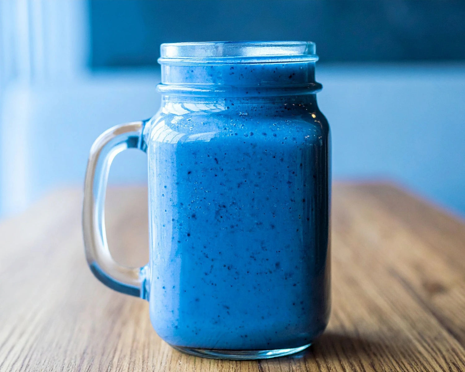 Blue smoothie in a glass jar with a handle on a wooden surface