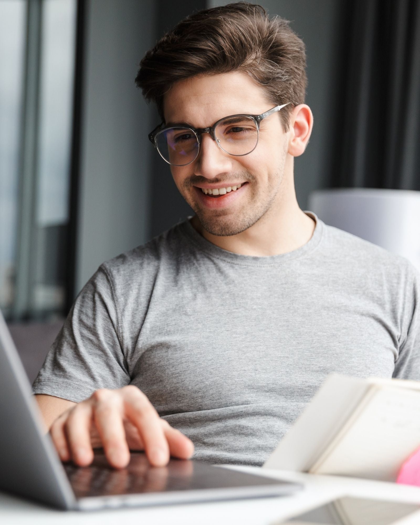 Man wearing glasses and a gray shirt using a laptop in an indoor setting