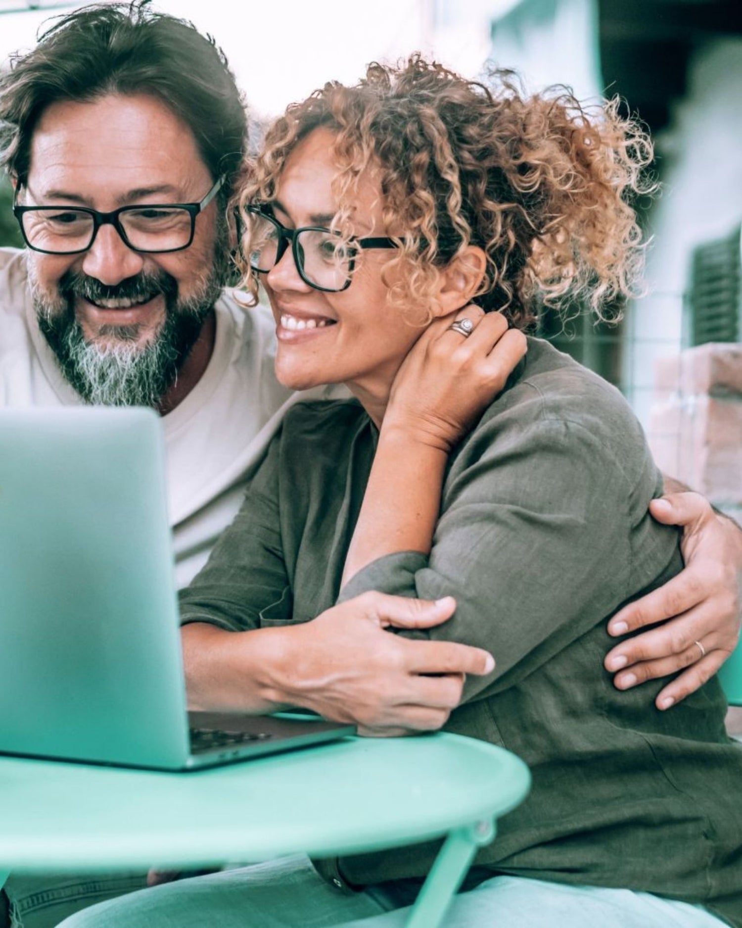 Two people sitting together, smiling and focused on a laptop screen.