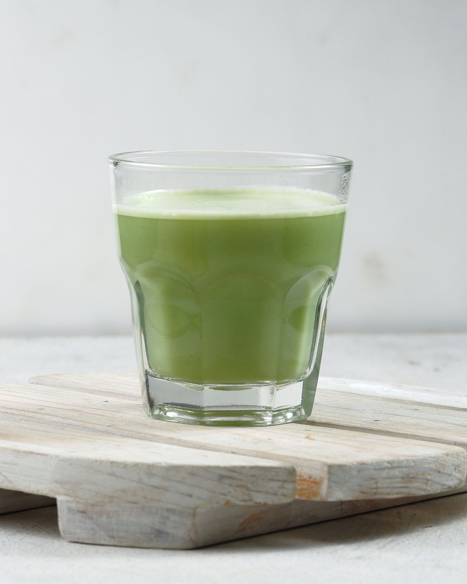 Clear glass filled with green liquid on a wooden surface with a white background