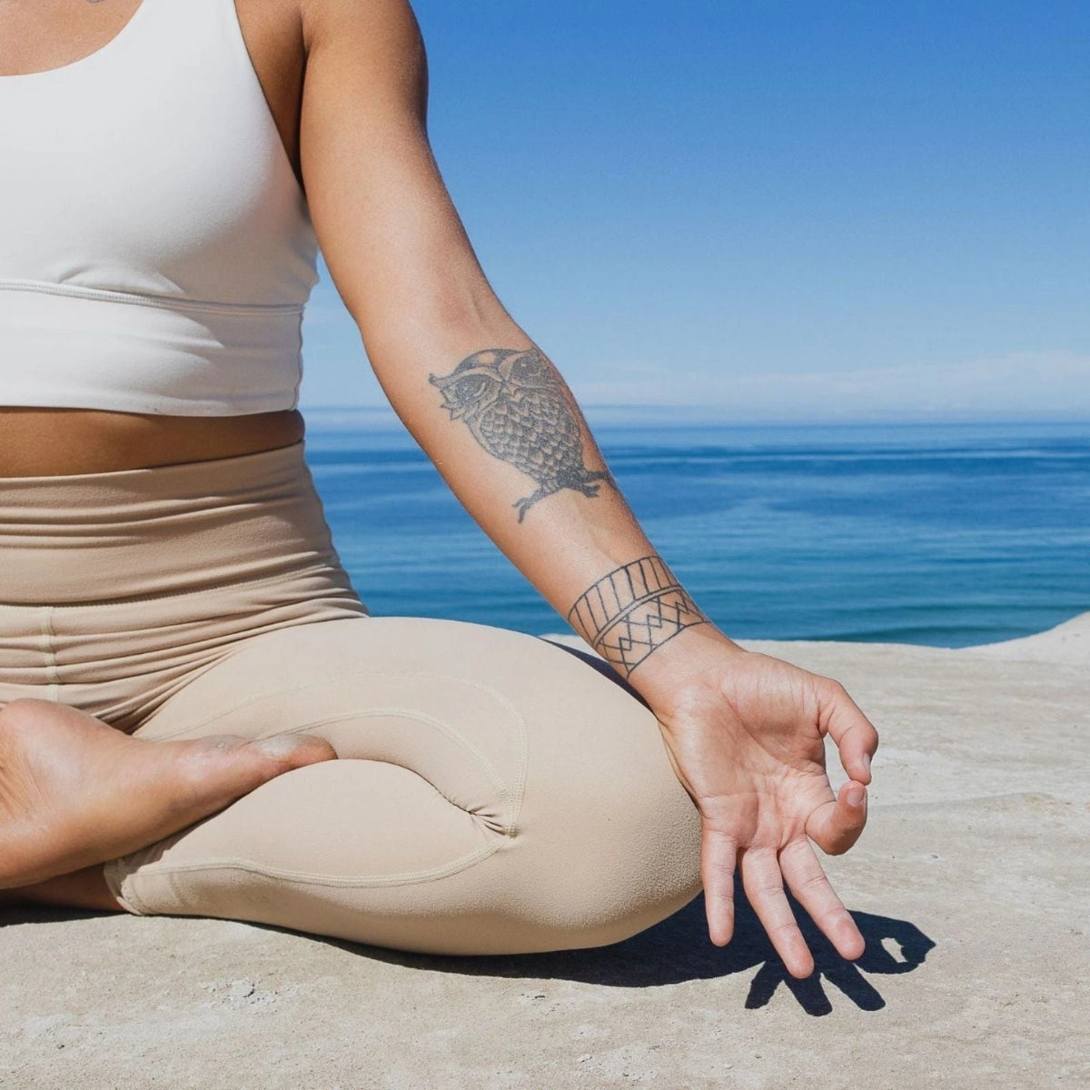 Person meditating on a beach with tattoos on their arm and hand.