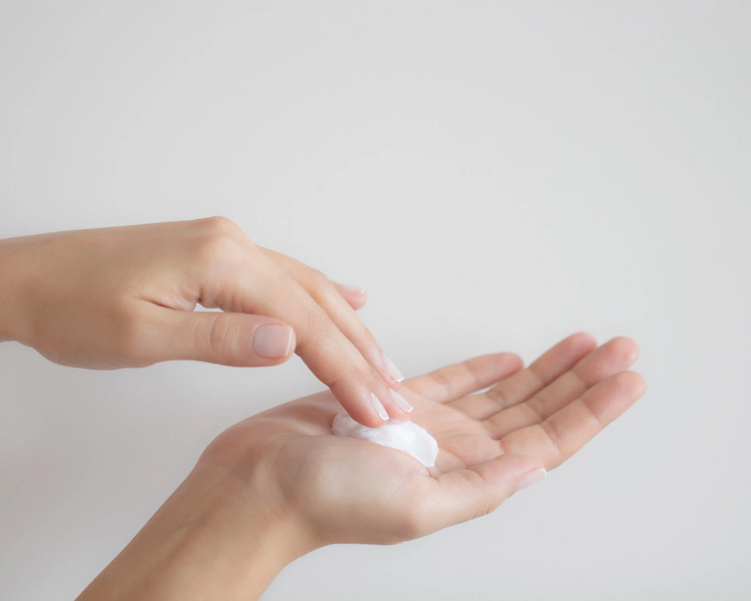 Two hands with a small amount of white cream on a light gray background