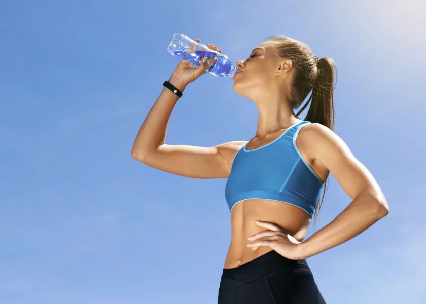Fit woman hydrating after a workout under a clear blue sky, representing natural energy and recovery support—highlighting the benefits of E3Live’s BlueMAJIK®, a nutrient-dense blue spirulina extract rich in phycocyanin to help fight inflammation, support joint health, and promote sustained vitality.