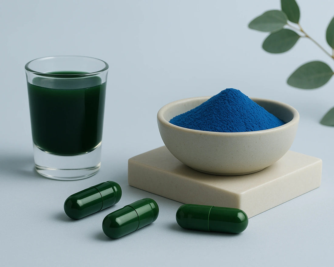 Blue powder in a bowl, green liquid in a glass, and green capsules on a light gray background with green leaves.
