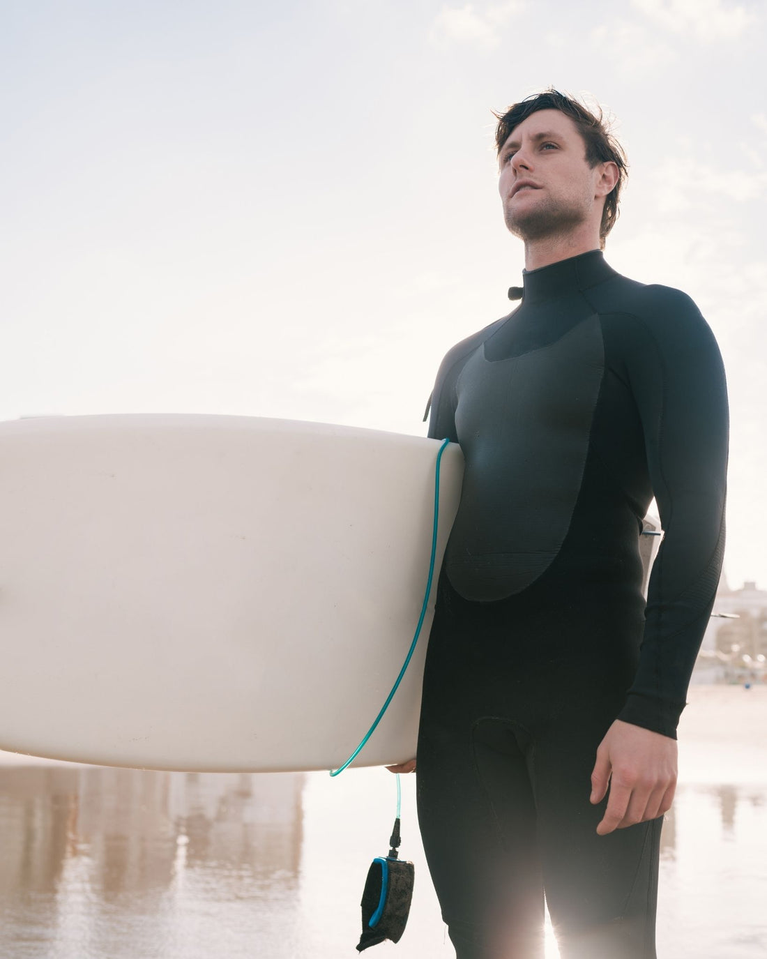 Man in a wetsuit holding a surfboard on a beach