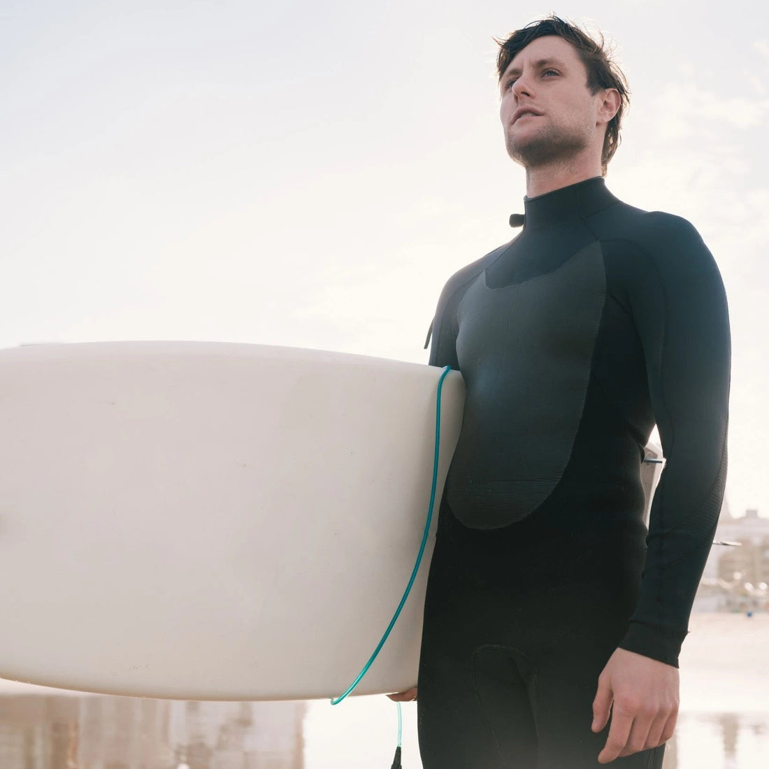 Man in a wetsuit holding a surfboard on a beach