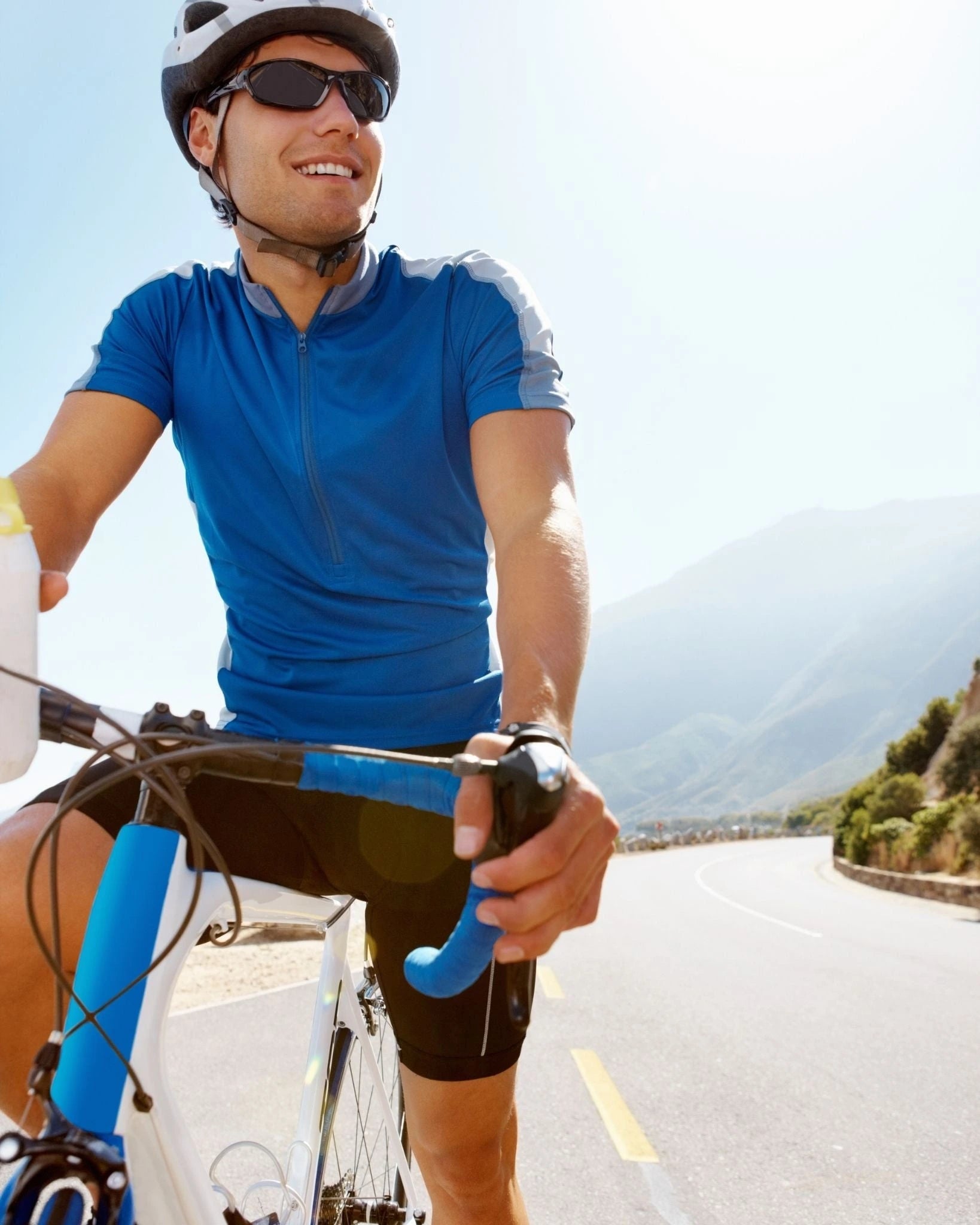 Man cycling on a road with mountains in the background