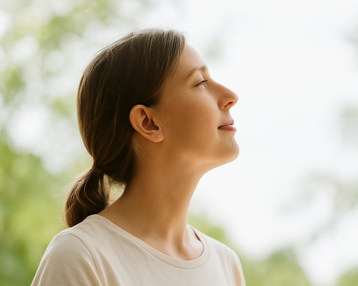 Woman with a ponytail looking upwards with a blurred natural background
