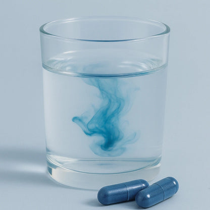 Clear glass of water with blue swirl and two blue capsules on a light gray background