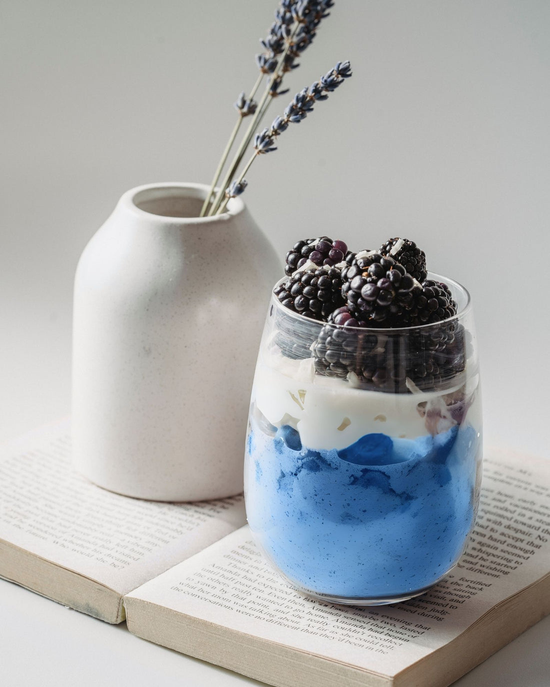 Glass of BlueMAJIK parfait with  blackberries on an open book with a white vase in the background