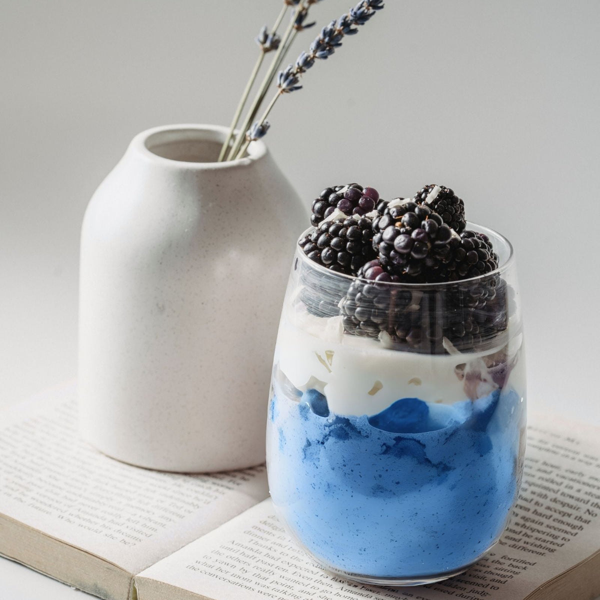 Glass of BlueMAJIK parfait with  blackberries on an open book with a white vase in the background