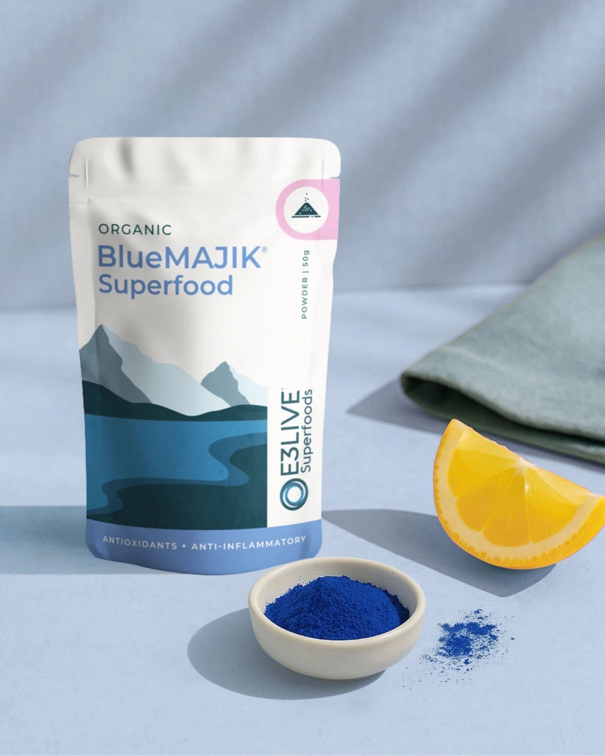 BlueMajik Superfood package with a bowl of blue powder and an orange slice on a light background