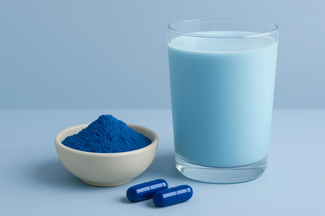 Blue powder in a bowl, blue capsules, and a glass of blue smoothie on a light blue background