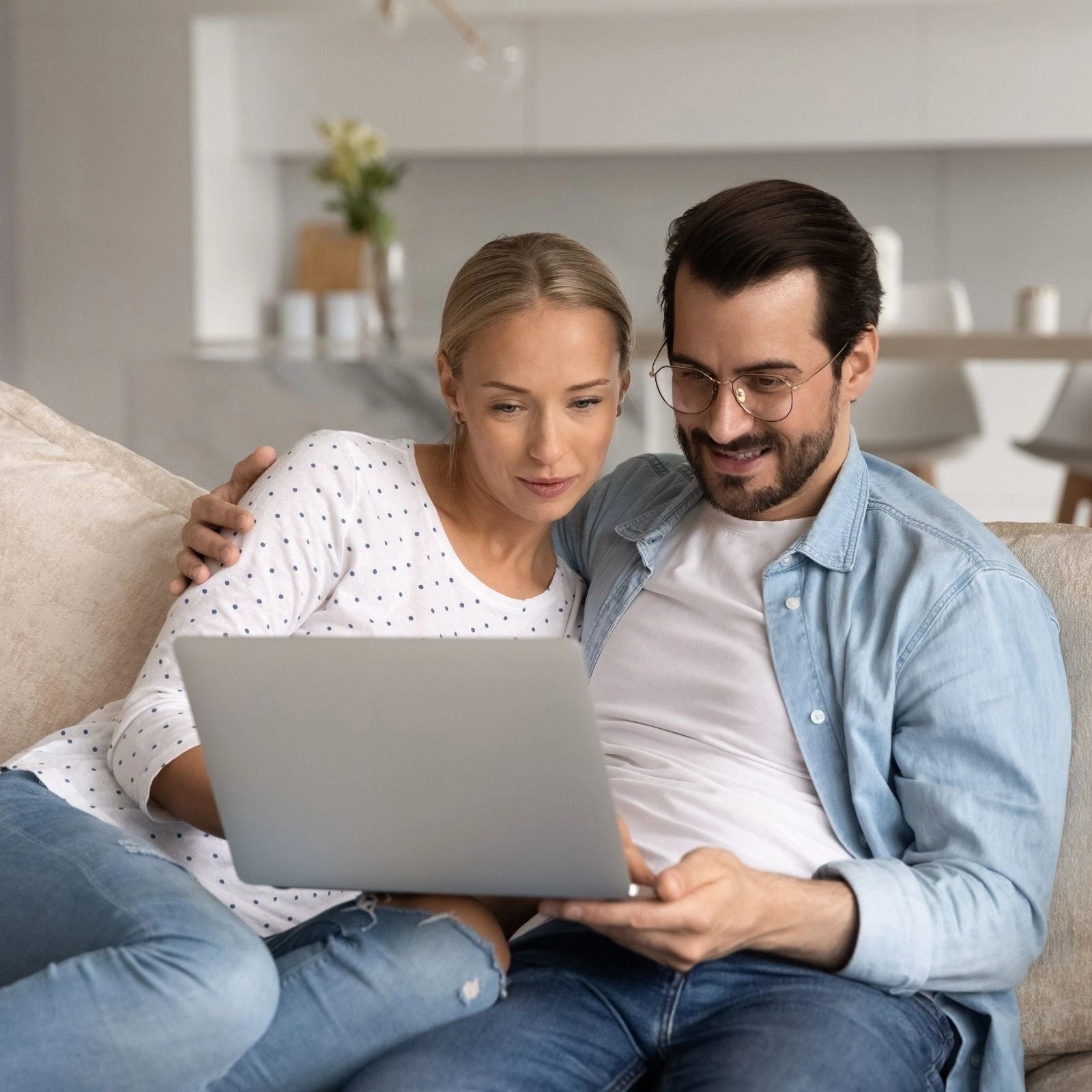 Man and woman sitting on a couch together, focused on a laptop in a home setting.
