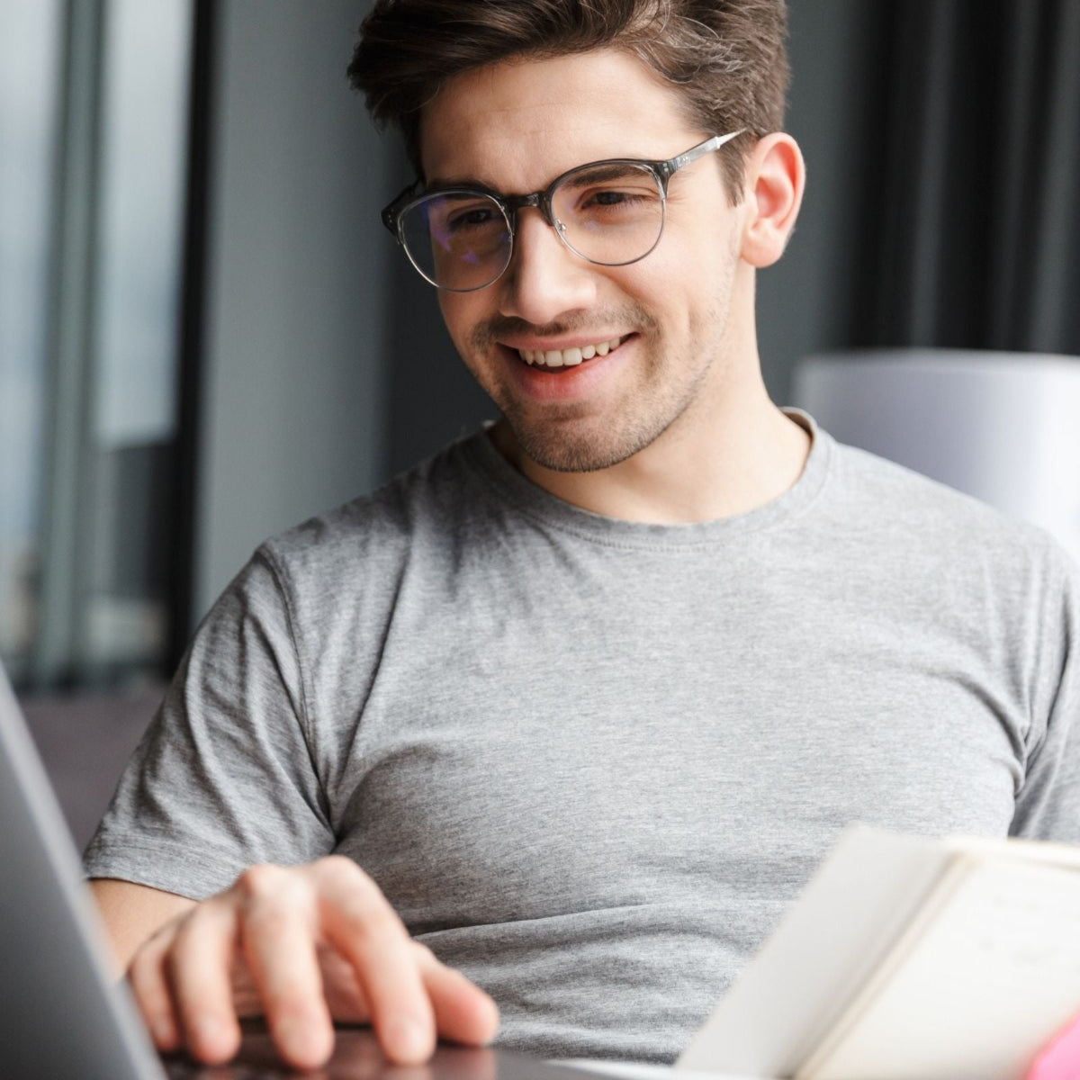 Man wearing glasses and a gray shirt using a laptop in an indoor setting