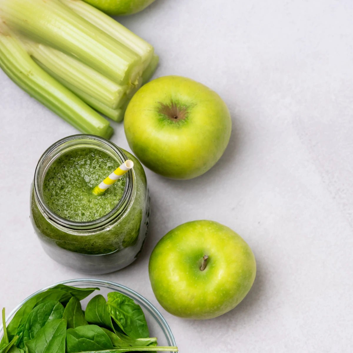 Green smoothie in a jar with celery, apples, and spinach on a light surface