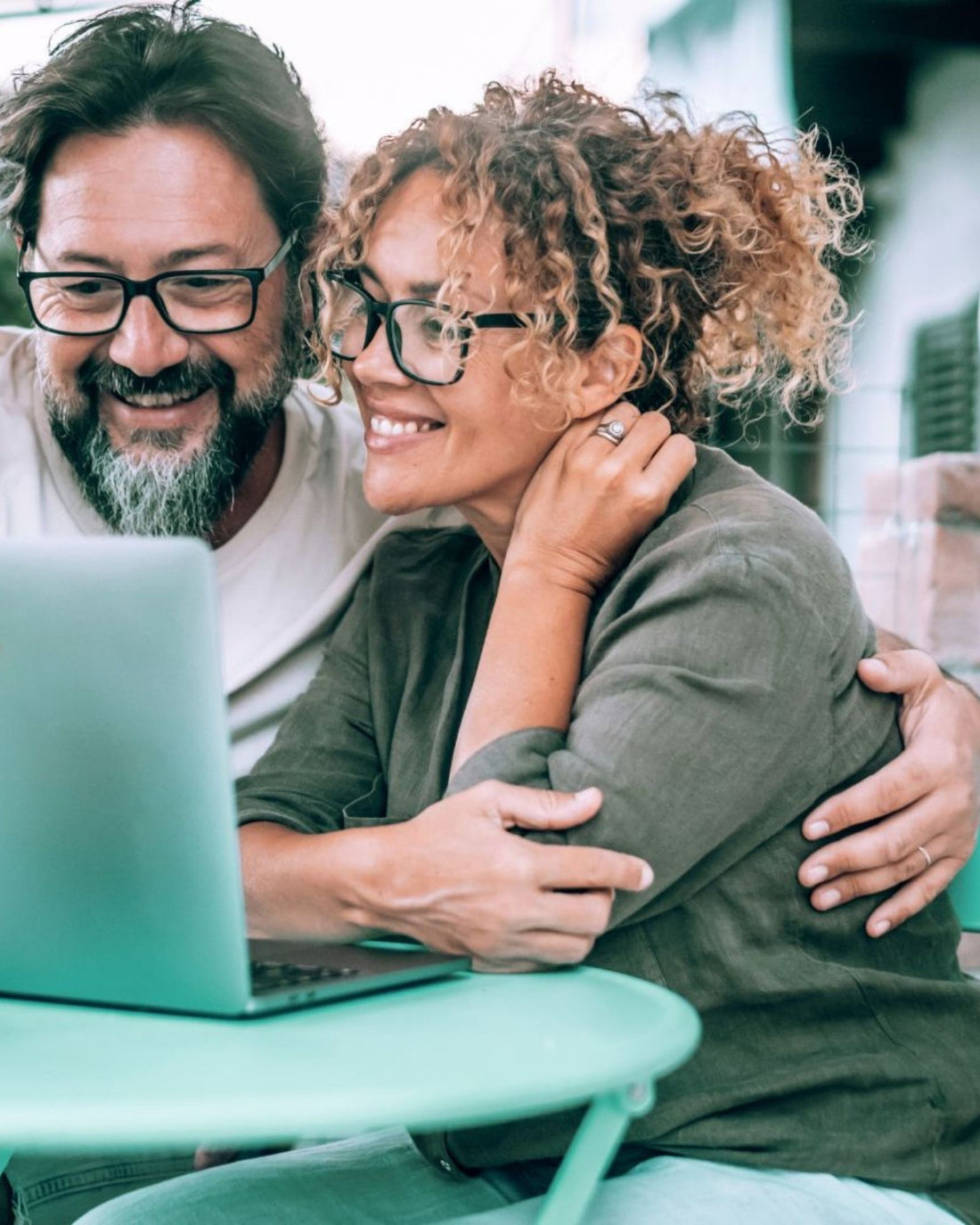 Two people sitting together, smiling and focused on a laptop screen.