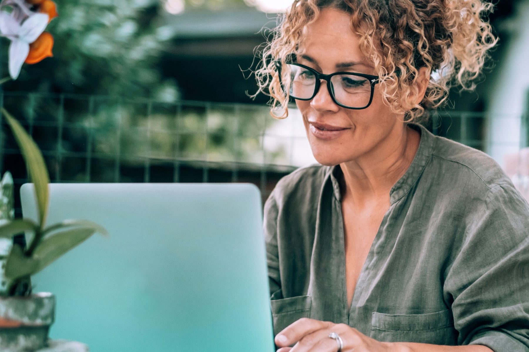 A thoughtful woman with curly hair and glasses using a laptop outdoors in a peaceful green environment, symbolizing enhanced focus and cognitive support, aligning with the BrainON collection.
