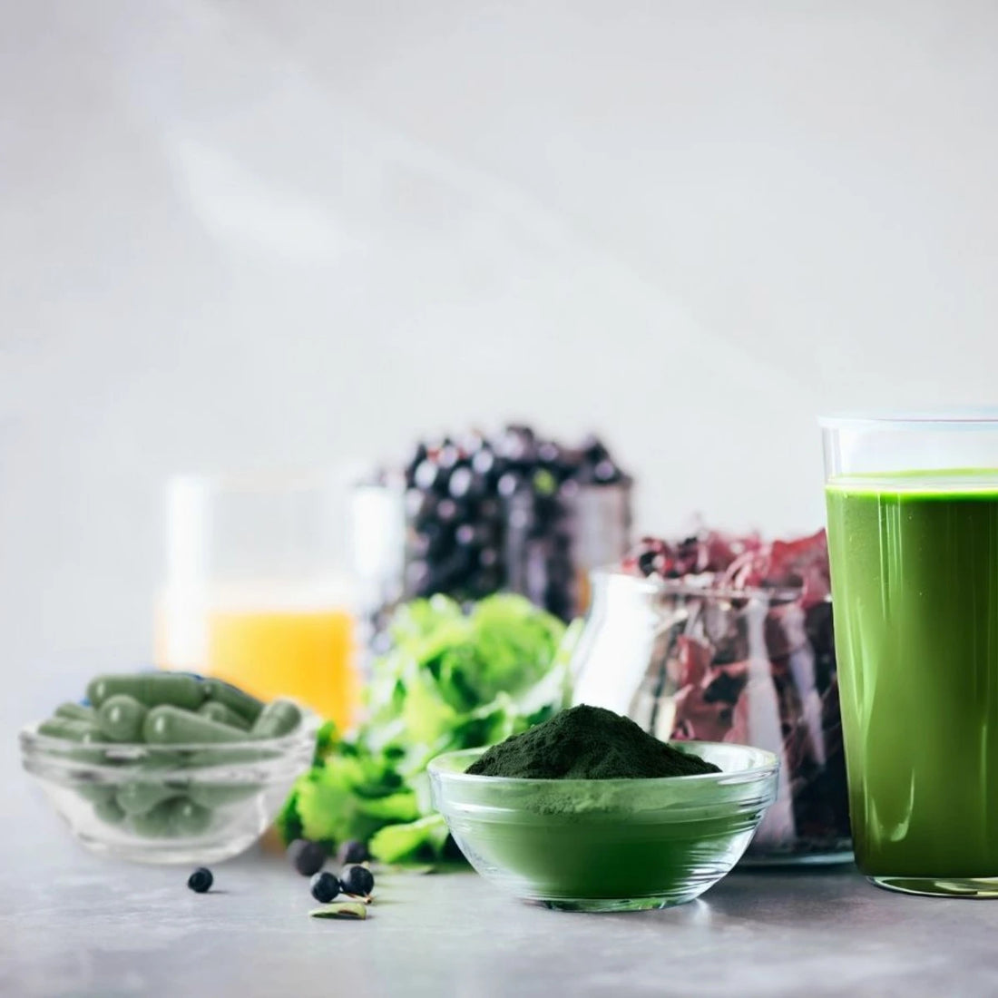 Green AFA powder in a bowl with a glass of green juice and other bowl with  green capsules on a light background