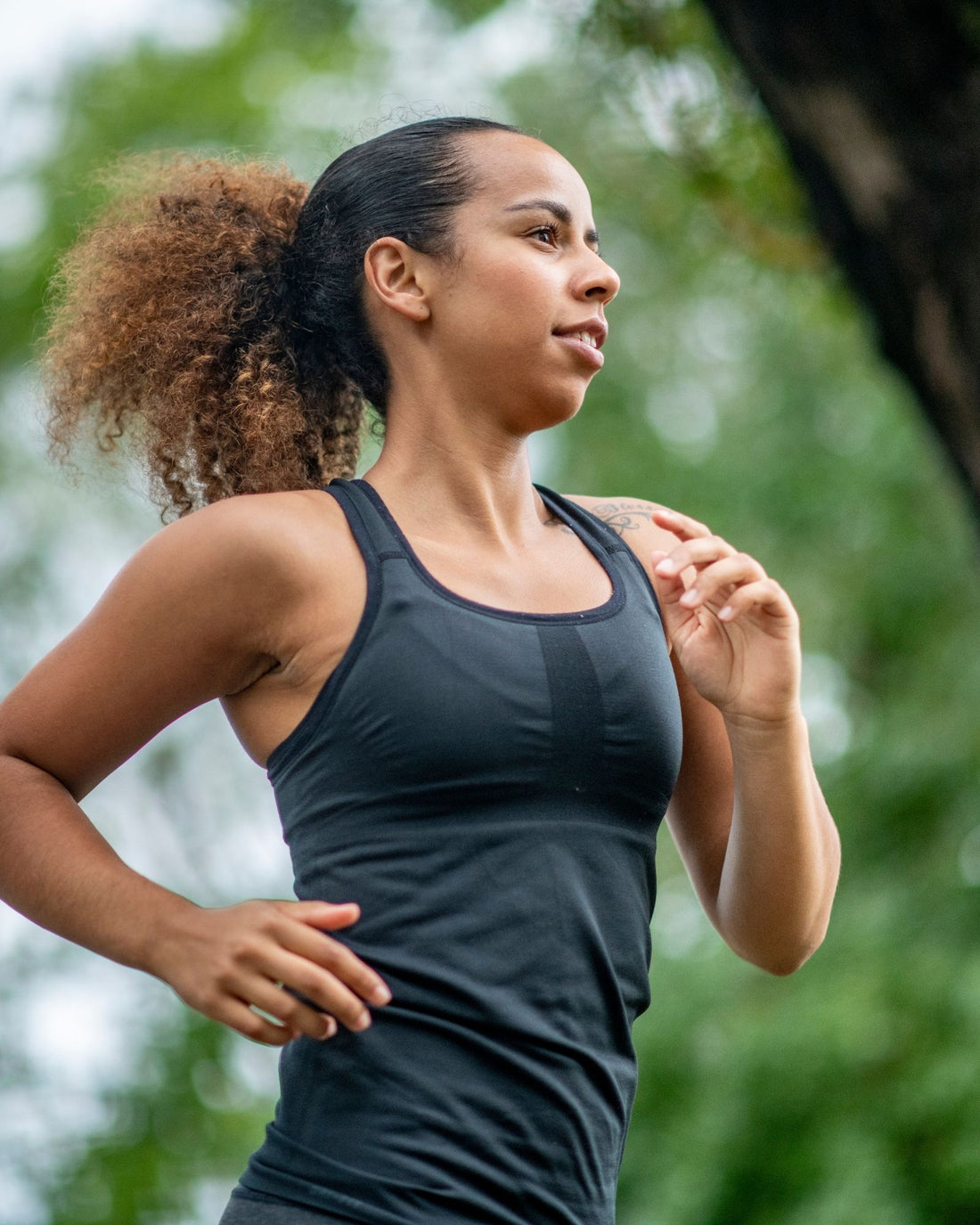Woman in a black tank top running outdoors with greenery in the background