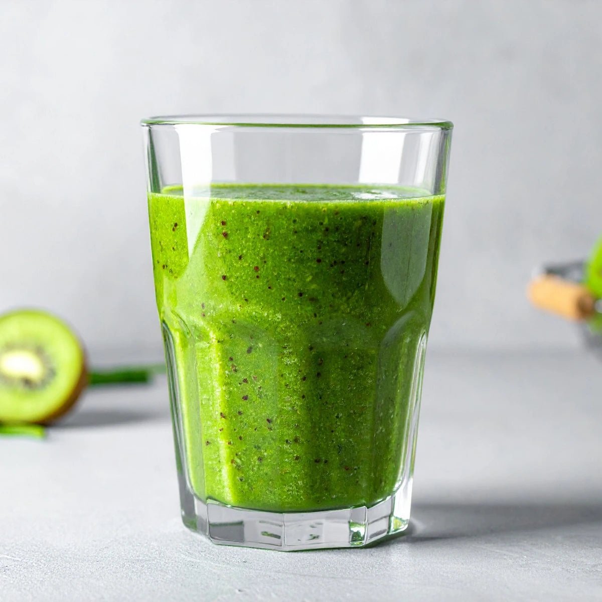 Green smoothie in a glass with a kiwi on a light background