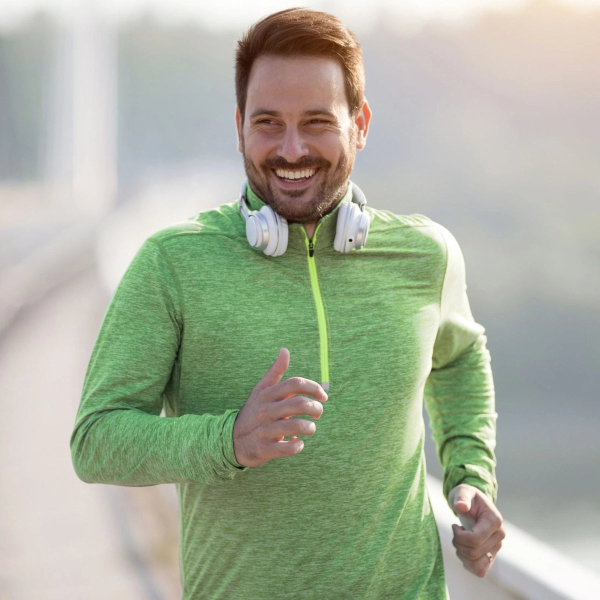 Man in green athletic jacket with white headphones jogging outdoors