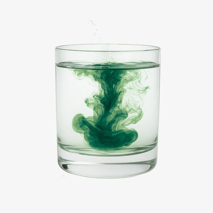 Clear glass with green powder swirling in water on a white background