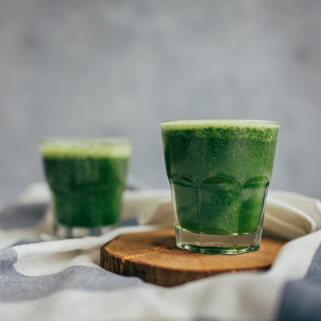 Two glasses of green juice on a wooden board with a grey background