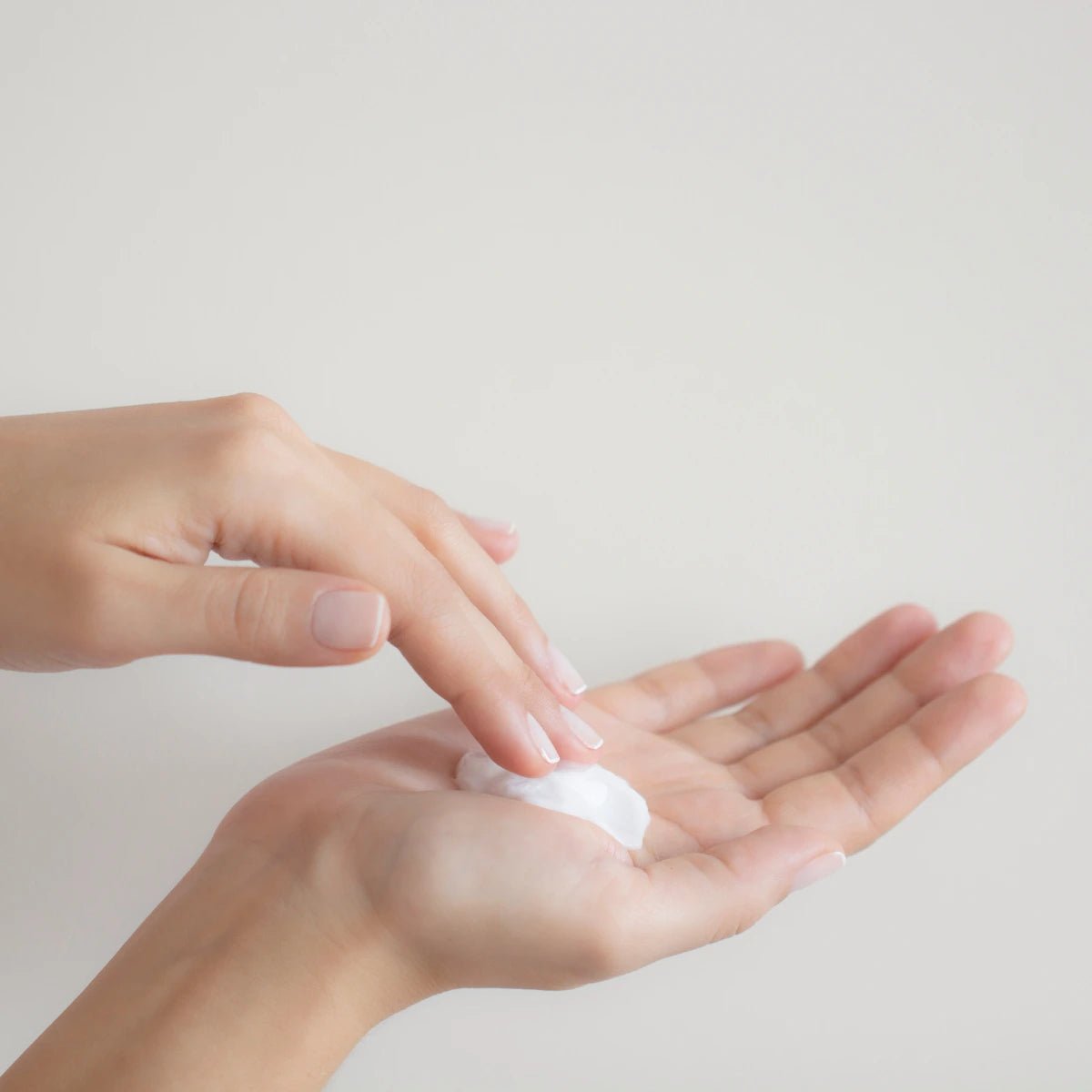 Person applying a small amount of cream to their palm against a light background