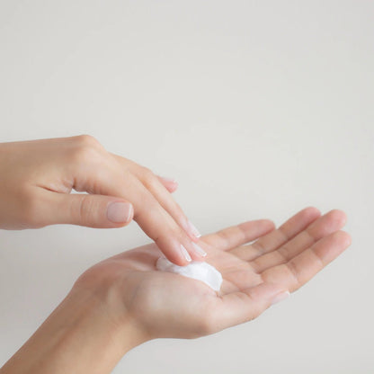 Person applying a small amount of cream to their palm against a light background