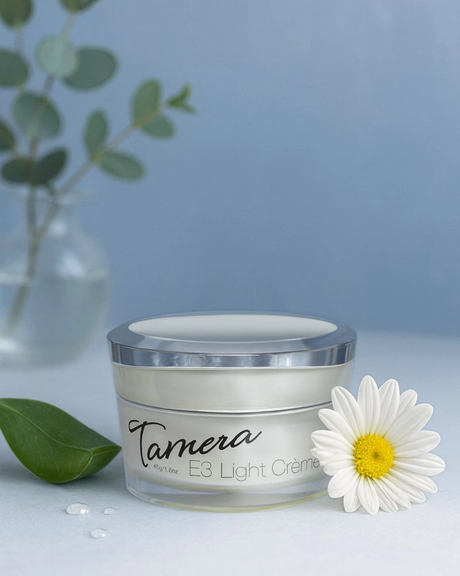 Jar of Tamera E3 Light Creme with a daisy and green leaves on a blue background