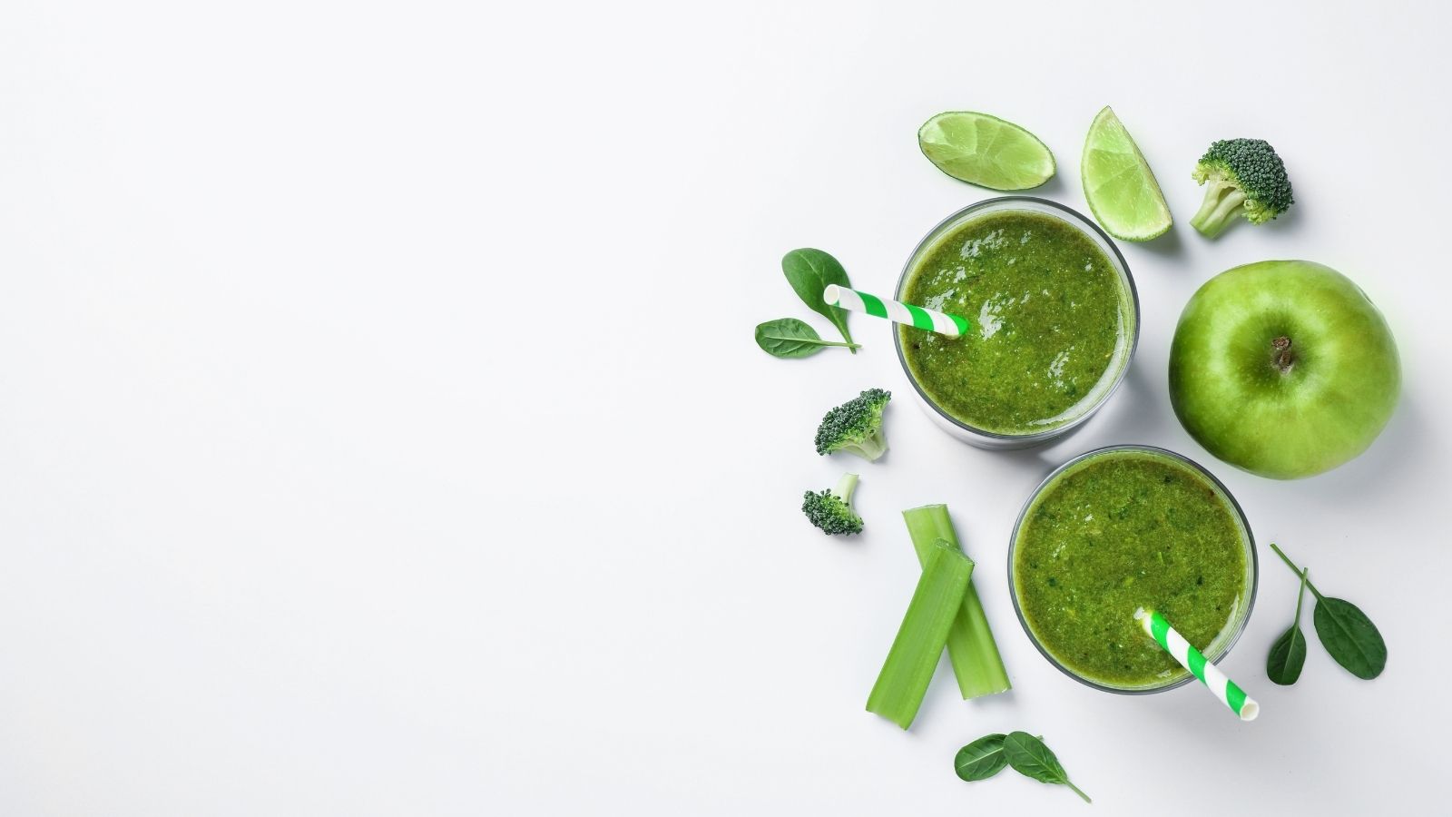 E3Live algae smoothies in glasses with straws, surrounded by green apples, broccoli, and spinach on a white background.