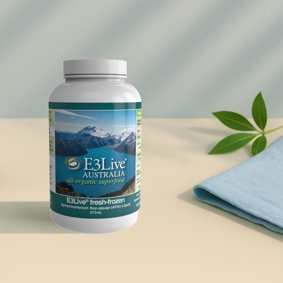 E3Live Australia supplement bottle on a beige surface with a light blue towel and green leaf.