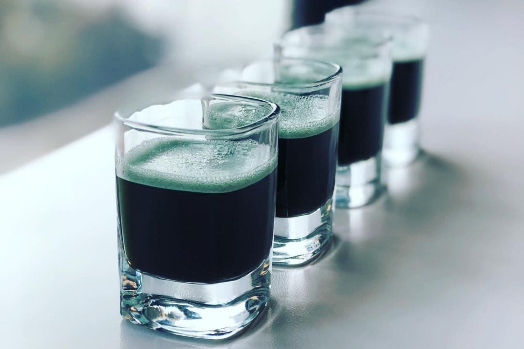 Four shot glasses with black bands containing a E3Live liquid on a light surface.