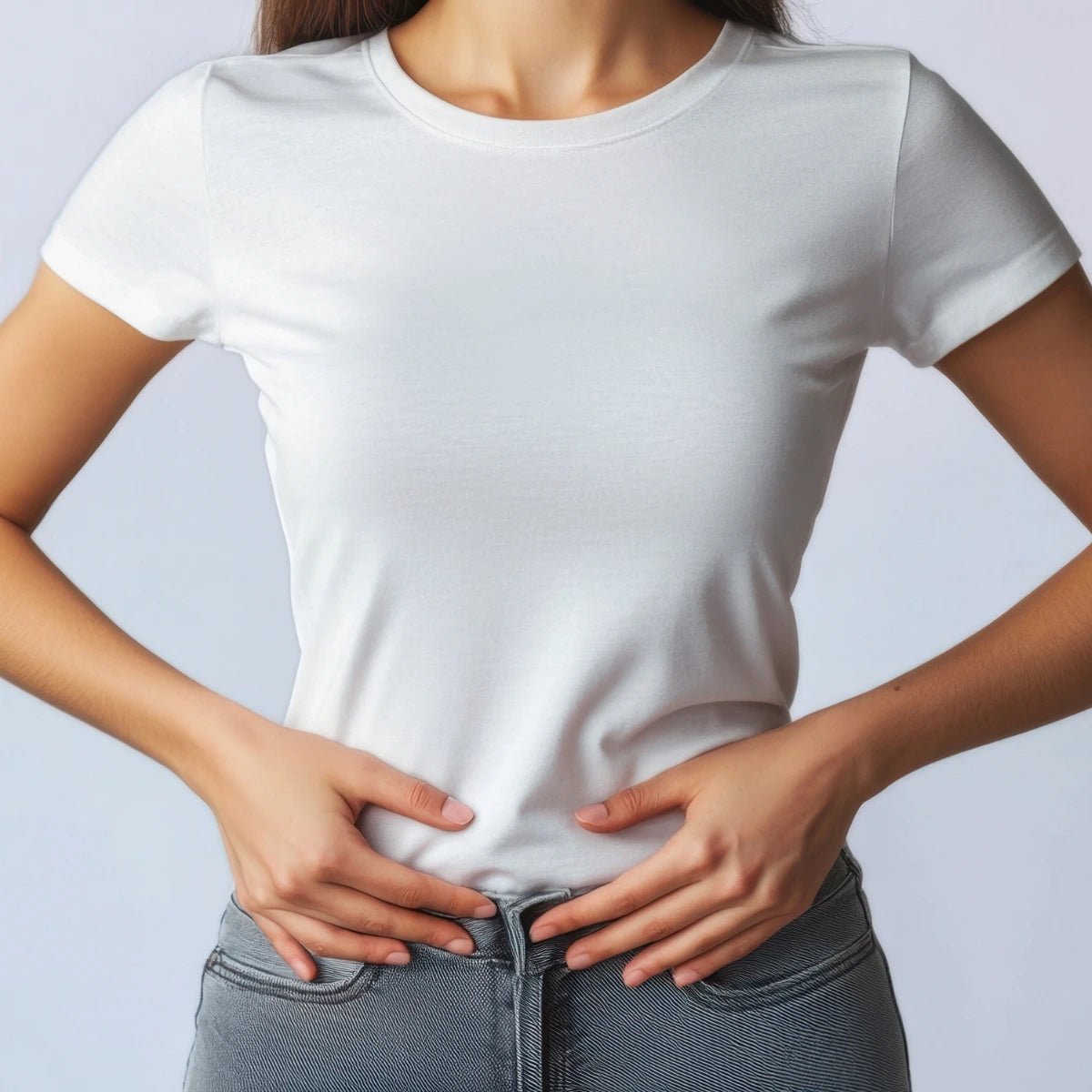 Person holding hands on stomach wearing a plain white t-shirt and jeans on a light gray background