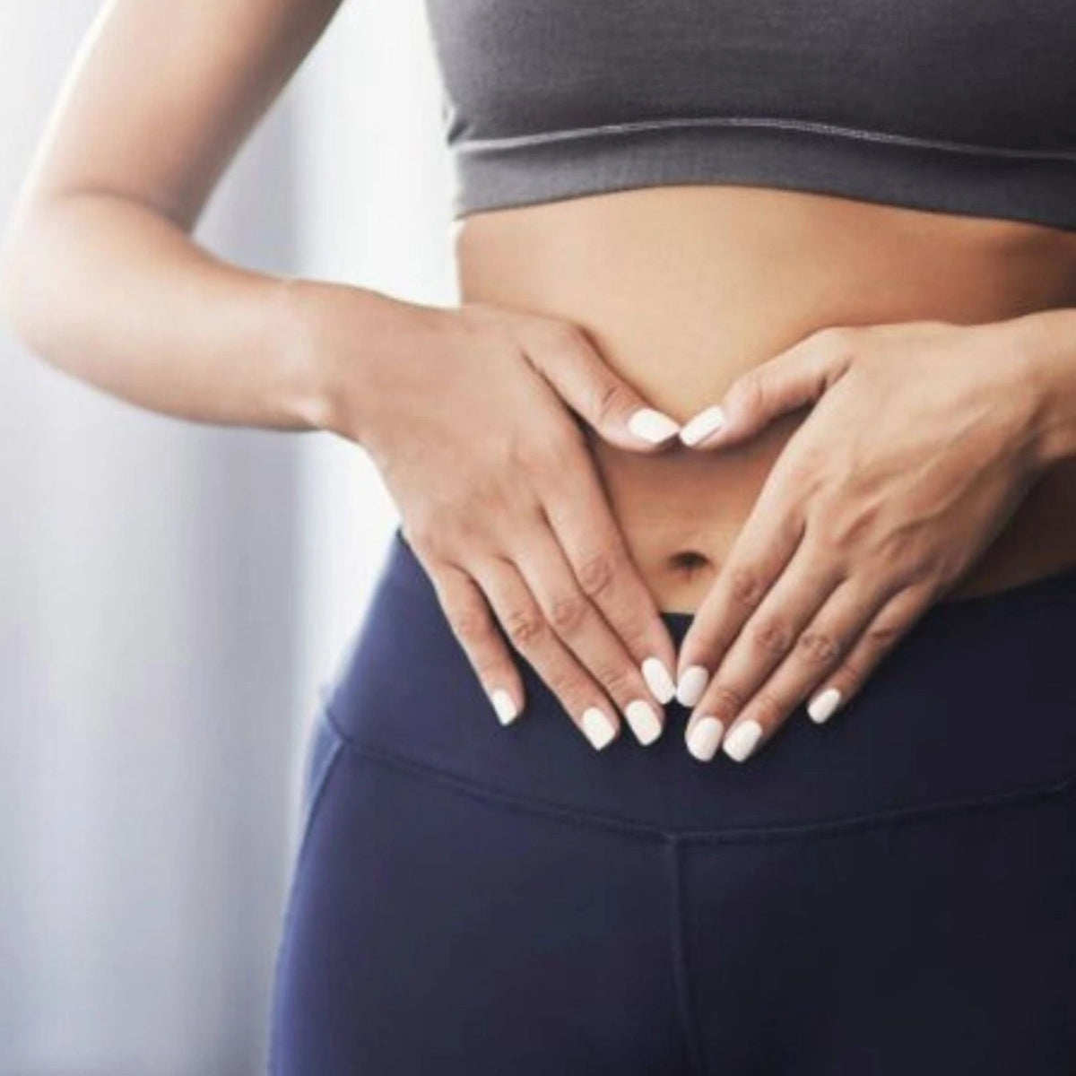 Person wearing a sports bra and leggings with hands on stomach