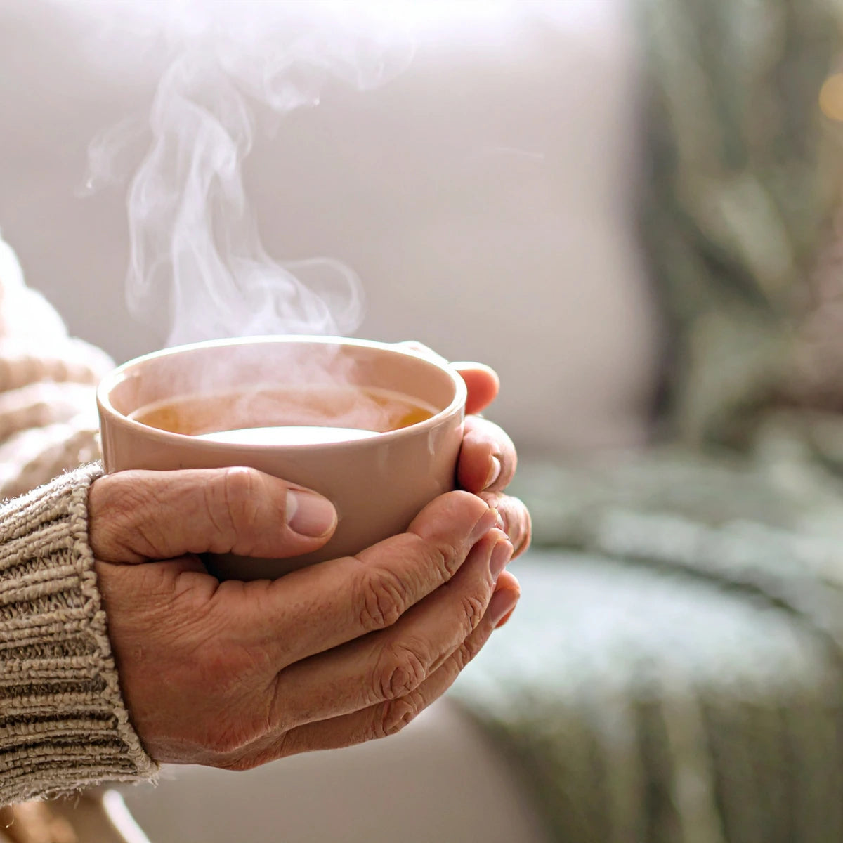 Hand holding a steaming cup of hot beverage with a blurred background