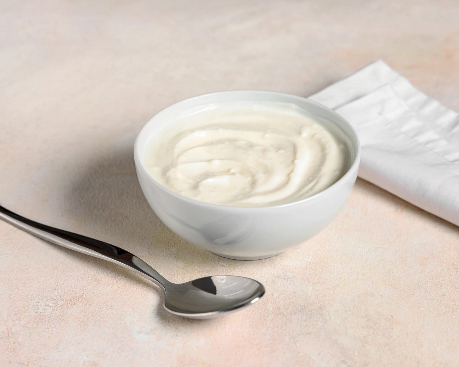 White bowl of yogurt with a spoon on a light surface