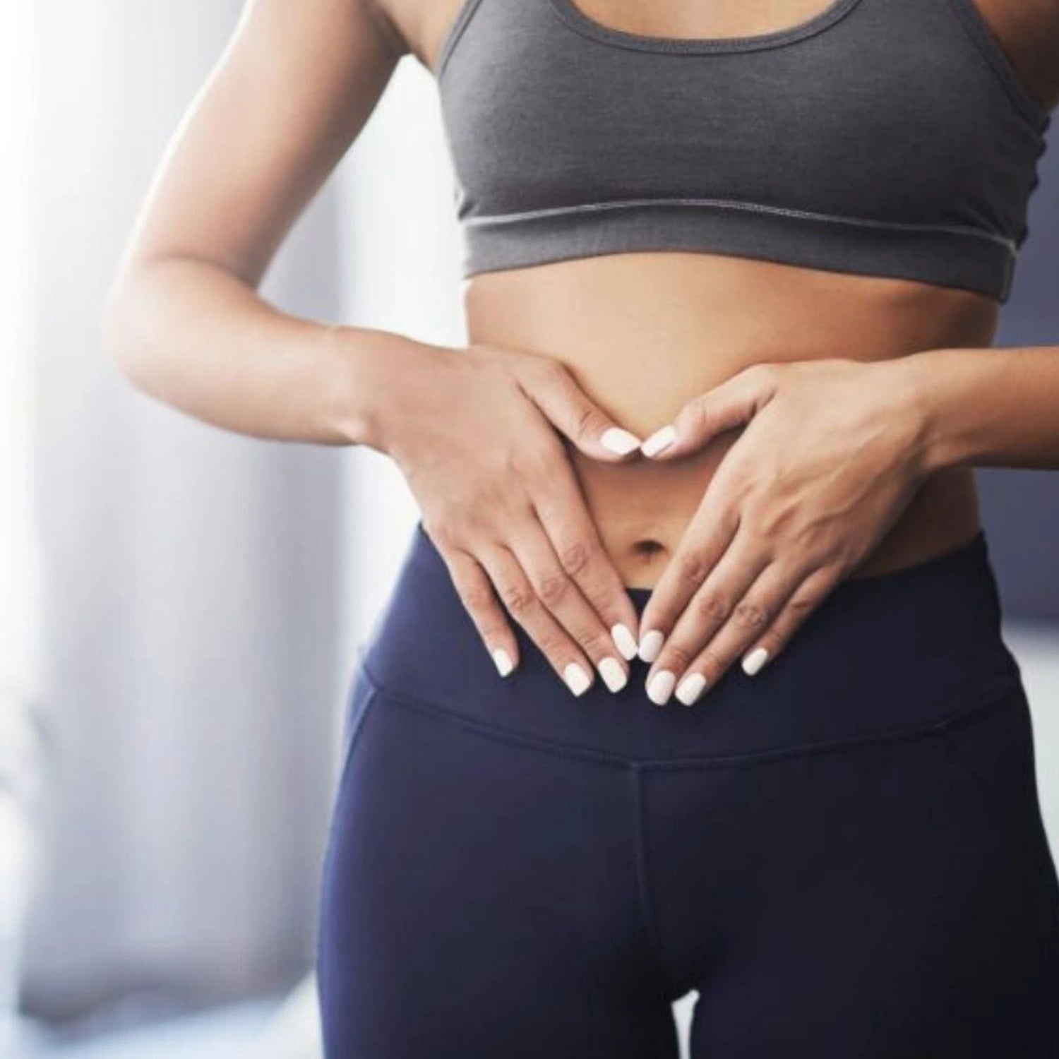 Person wearing a gray sports bra and dark blue leggings with hands on stomach.