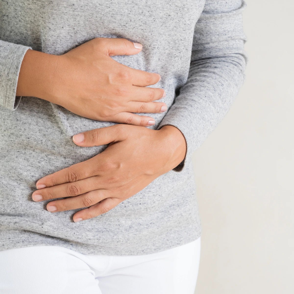 Person wearing a gray sweater with hands on stomach on a light background