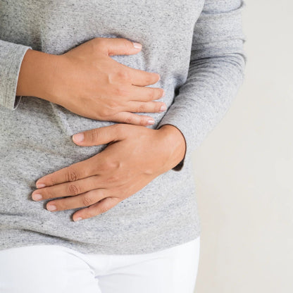 Person wearing a gray sweater with hands on stomach on a light background