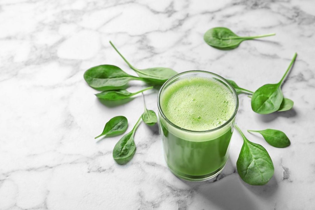 Glass of green juice with spinach leaves on a marble surface