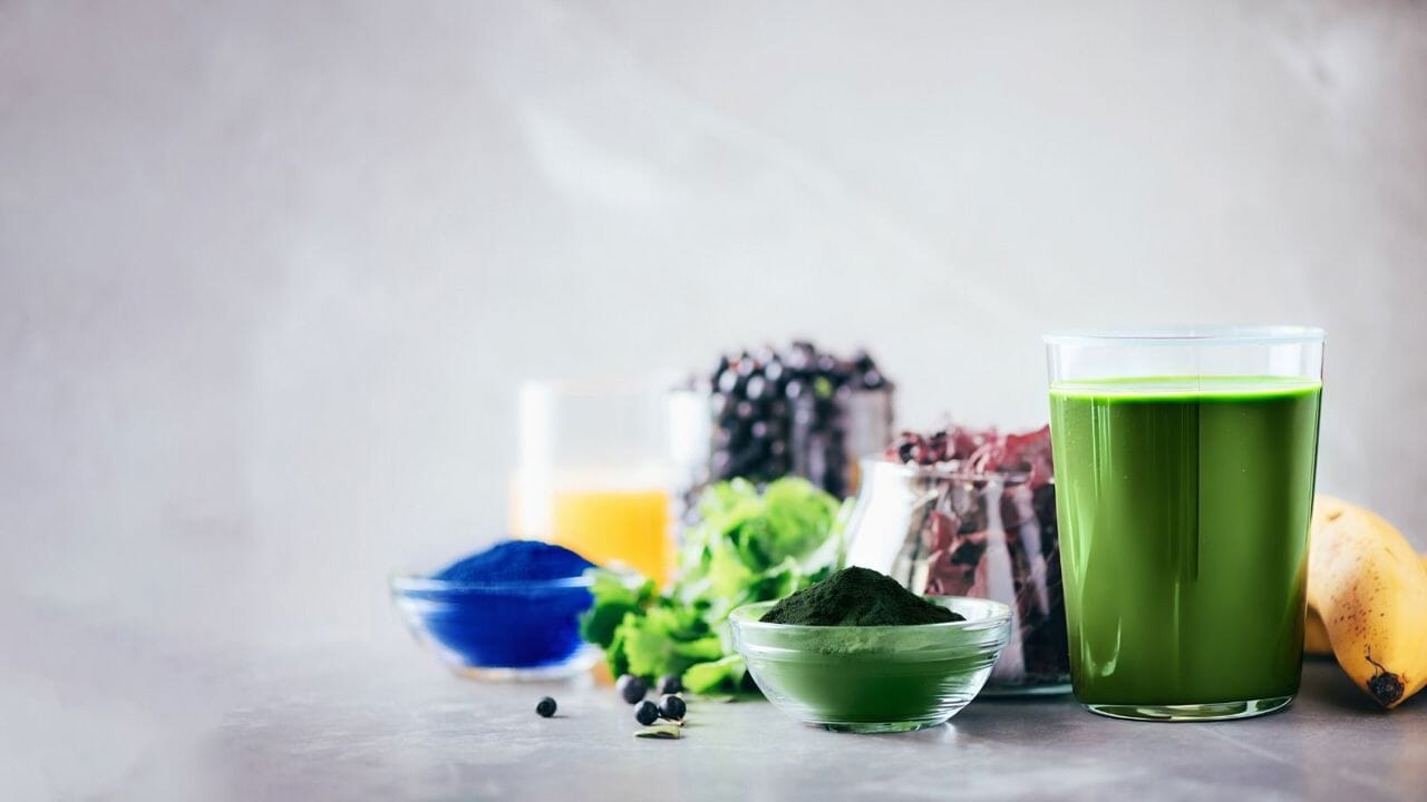 Green smoothie in a glass with ingredients like spinach and banana on a light background