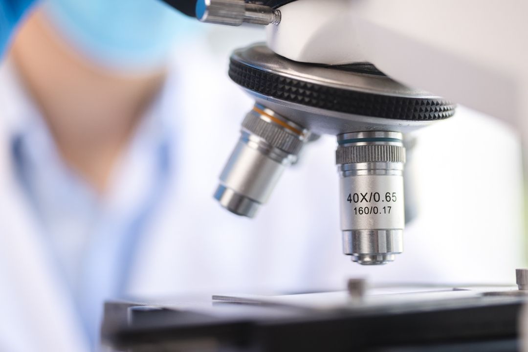 Microscope with a person wearing a lab coat in the background