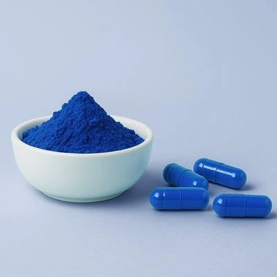 BlueMAJIK powder in a bowl with blue capsules on a light blue background