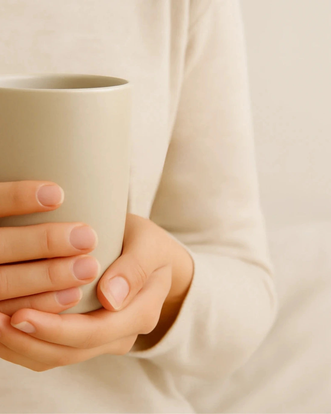 Person holding a beige ceramic mug with a soft focus background