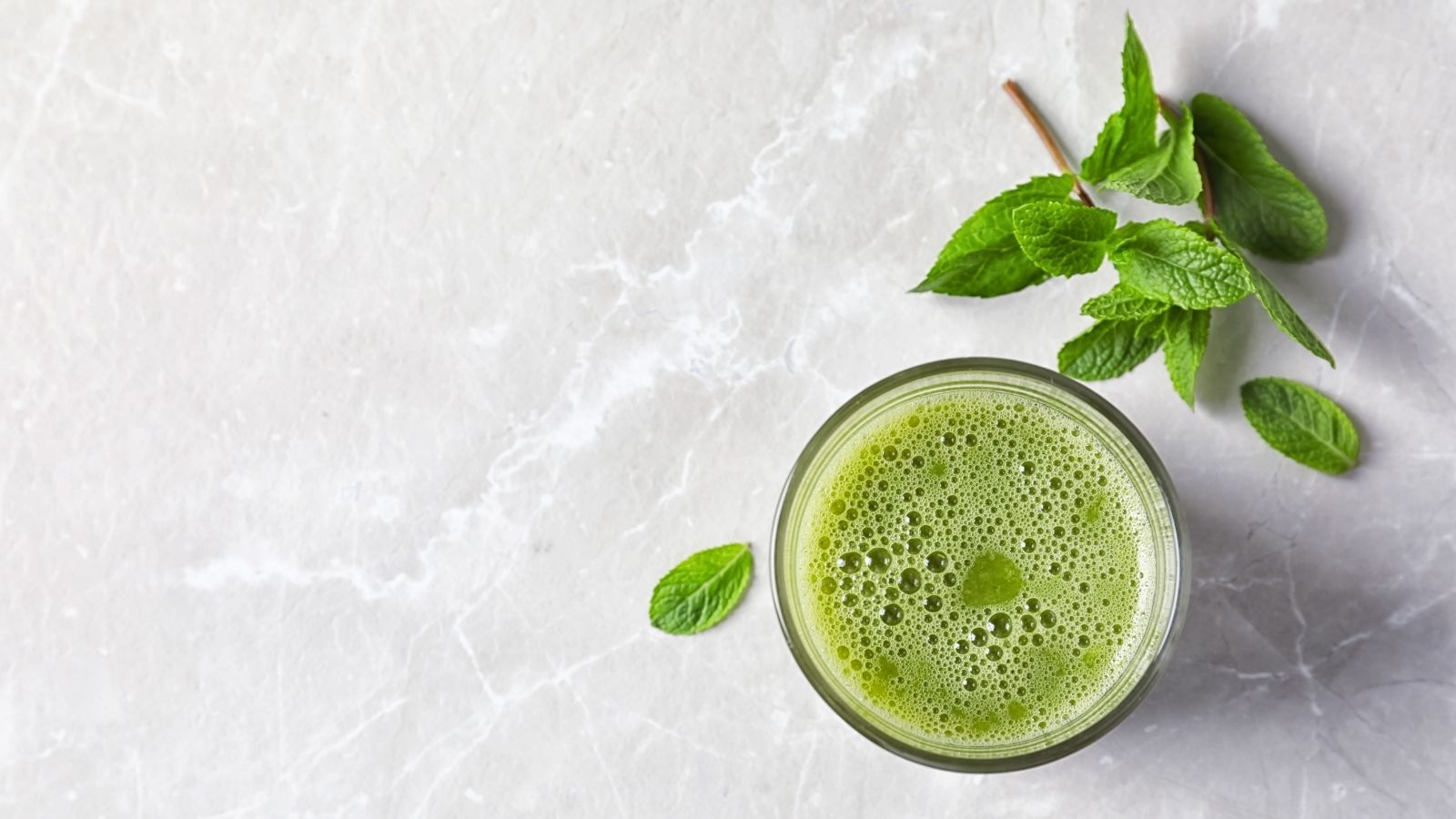 Green smoothie in a glass with mint leaves on a light gray background