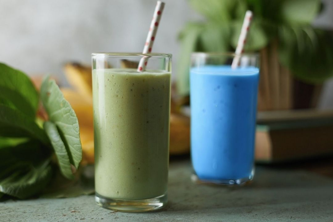 Two smoothies in glasses on a table, one green (E3AFA) and one blue (BlueMAJIK).