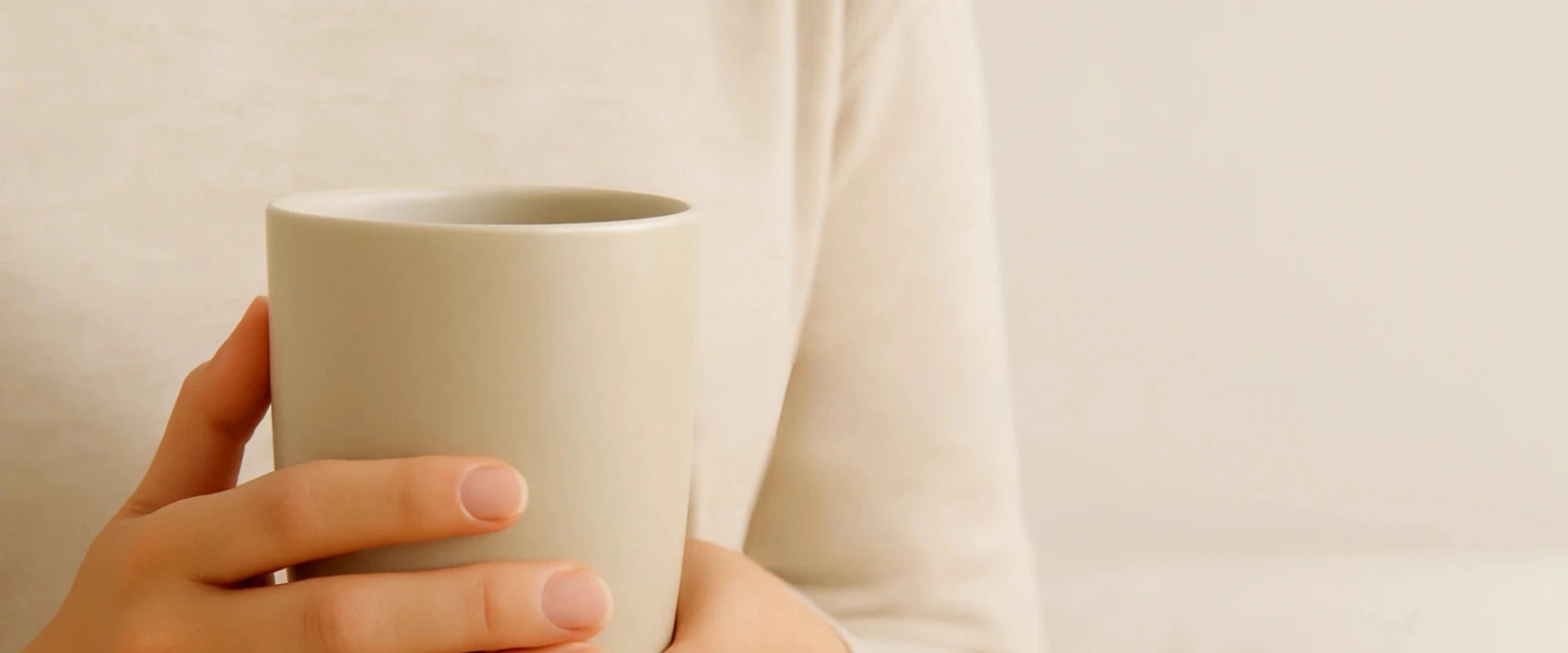 Person holding a white ceramic mug against a plain background